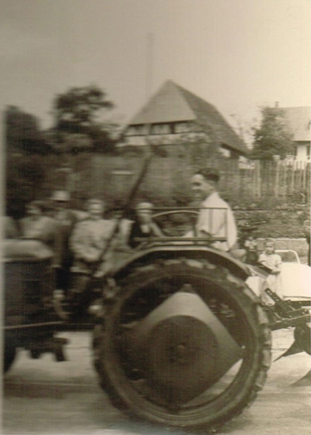 Roland Arnold auf Deutz mit Pflug beim Heimattag 1957. Die Menschen am linken Bildrand verdecken den Brunnen. Hinten in der Mitte ist die Pfarrscheune zu sehen, hinten rechts das Pfarrhaus.